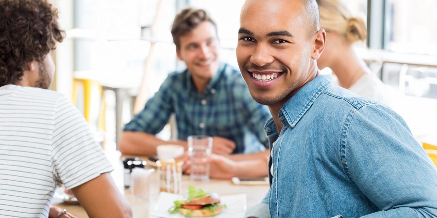 Portrait of happy african young man with his friends eating at c happy man in cafeteria