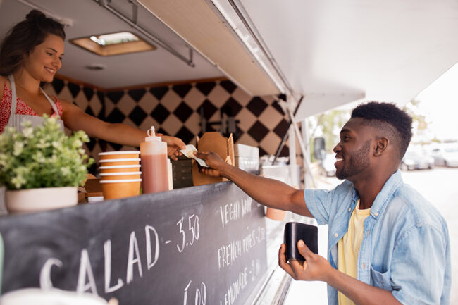 african american man buying wok at food truck street sale, payment and people concept - happy african american young man buying wok and paying with dollar money at food truck