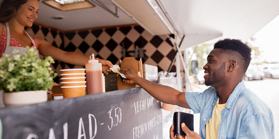 african american man buying wok at food truck street sale, payment and people concept - happy african american young man buying wok and paying with dollar money at food truck