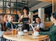 Young african american woman waitress taking orders from clients in cafe