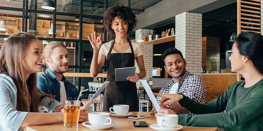 Young african american woman waitress taking orders from clients in cafe