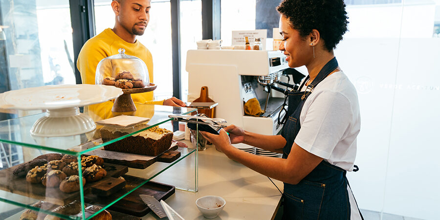 Bakery, happy portrait of black woman in cafe ready for serving pastry, coffee and baked foods. Restaurant, coffee shop and confident waiter barista by counter for service, help and welcome