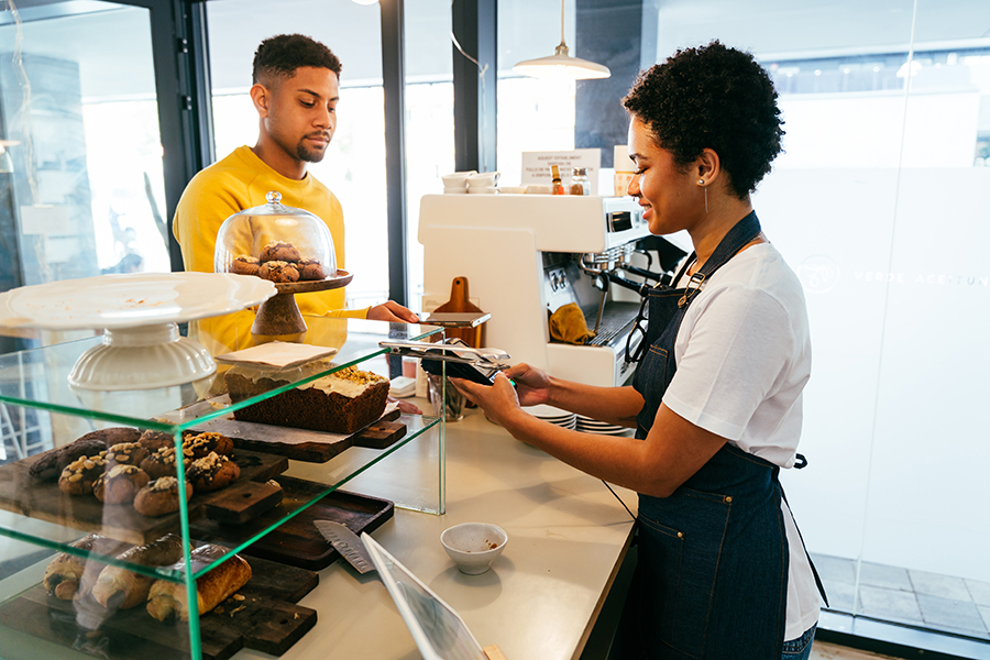 Bakery, happy portrait of black woman in cafe ready for serving pastry, coffee and baked foods. Restaurant, coffee shop and confident waiter barista by counter for service, help and welcome