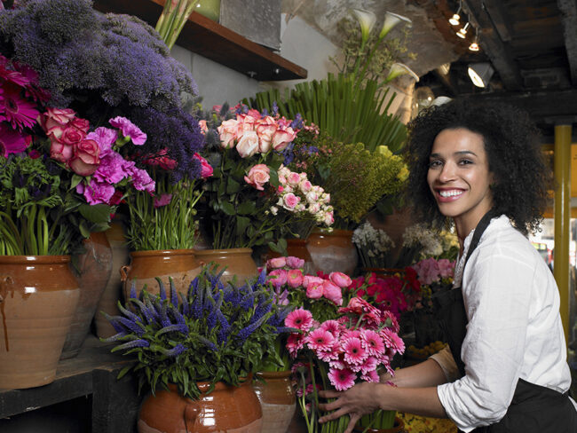 Florist with a radiant smile surrounded by colorful blooms in a cozy flower shop.
