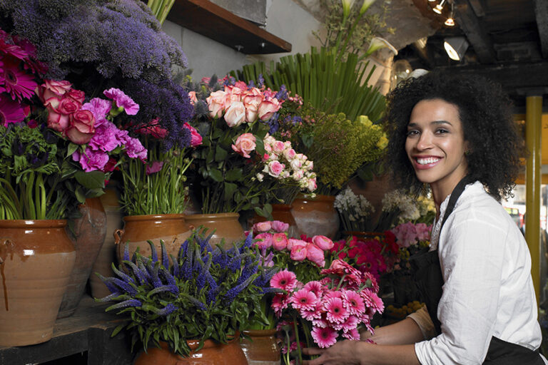 Florist with a radiant smile surrounded by colorful blooms in a cozy flower shop.